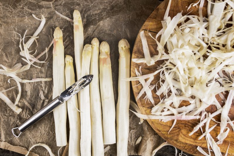 Shelled white asparagus with peelings on brown crumpled paper