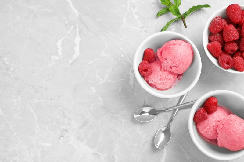 Flat lay composition with delicious raspberry ice cream on grey marble table, space for text