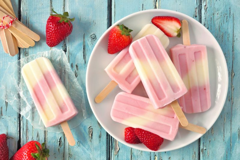 Healthy strawberry yogurt ice pops on a plate, top view summer table scene against a blue wood background