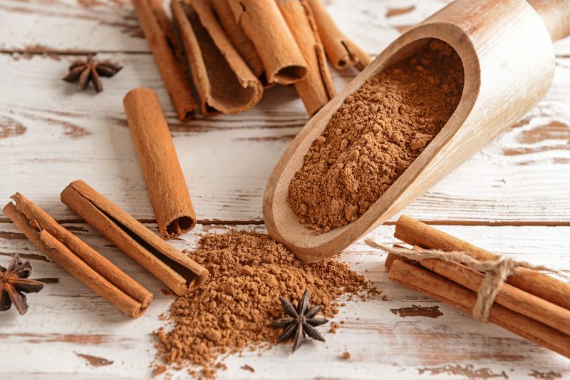 Scoop with cinnamon powder and sticks on light wooden background