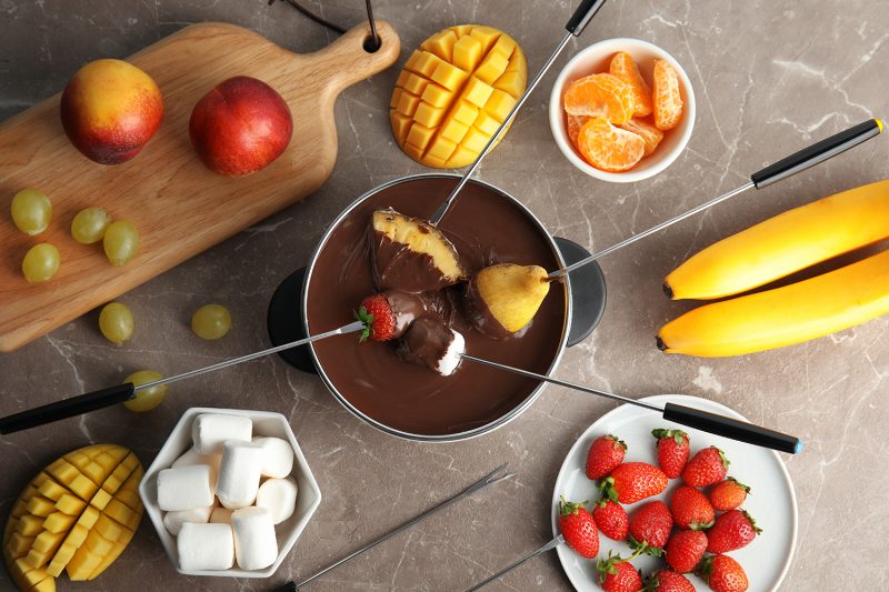 Flat lay composition with chocolate fondue in pot and fruits on gray background