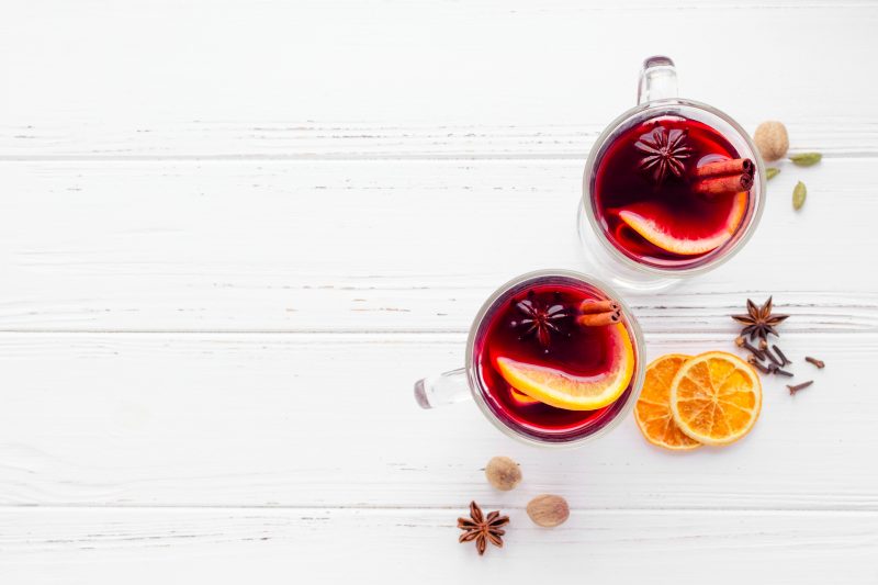 Two glasses of hot red mulled wine or gluhwein with orange, cinnamon sticks and anise on white wooden background. Spicy warm beverage. Seasonal mulled drink. Top view. Copy space.