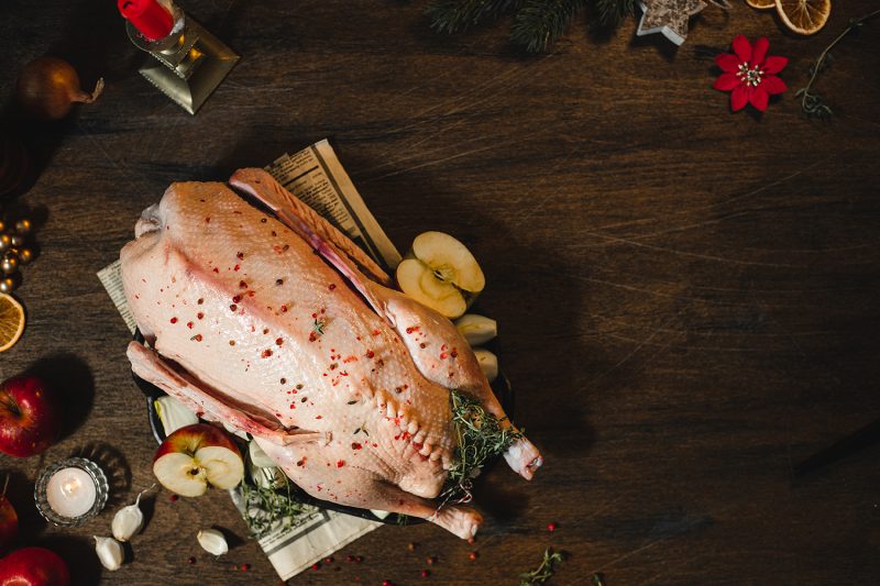 Directly above shot of a raw Christmas duck ready to cook with thyme and apples on a wooden table. Cooking christmas dinner in kitchen.