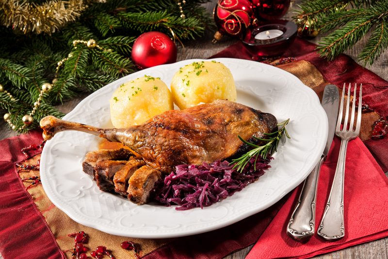Crusty goose leg with braised red cabbage and dumplings on Christmas decorated table