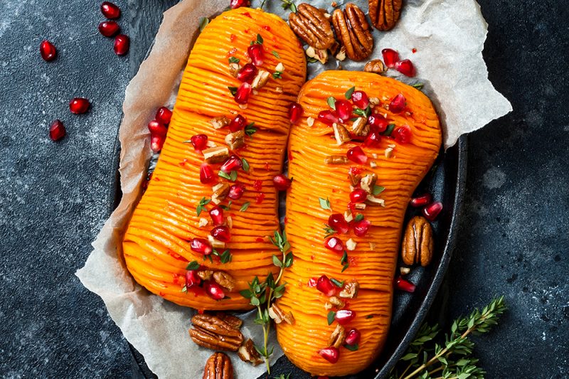 Roasted hasselback butternut squash pumpkin with thyme, pecan and pomegranate. Thanksgiving dinner recipe. Vegan healthy seasonal fall or autumn food